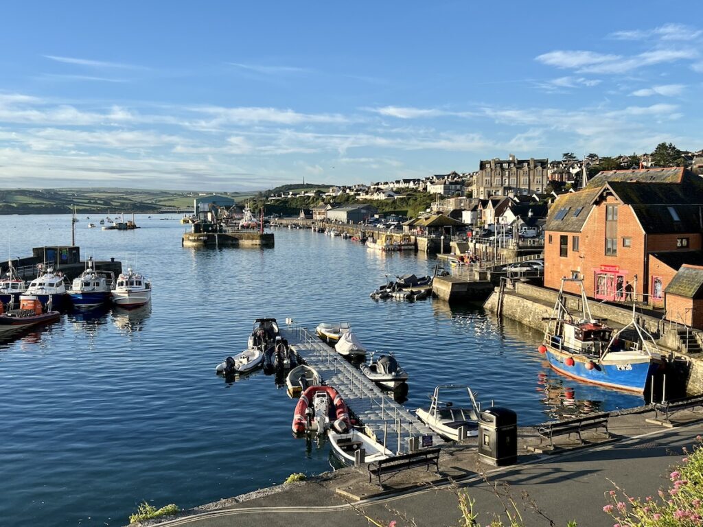 Sunlit Padstow harbor with fishing boats docked beside the lively quayside, showcasing the coastal charm of Padstow, Cornwall